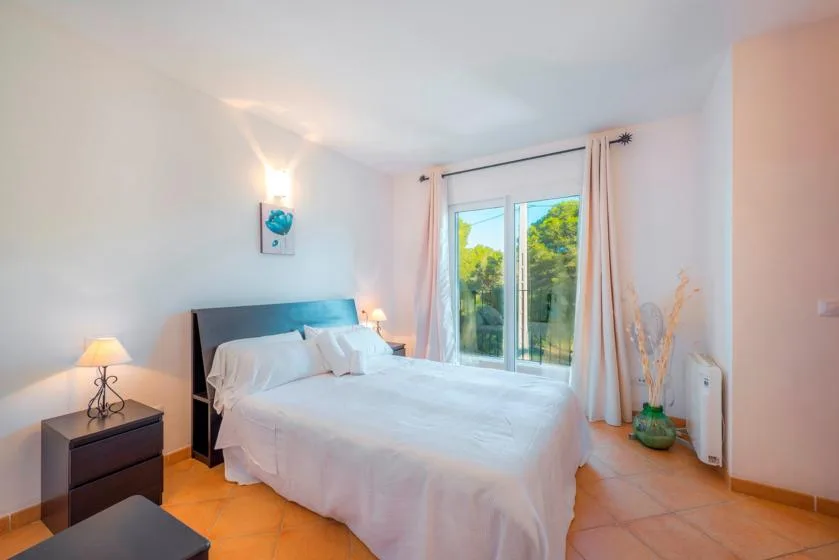 A bright bedroom with a neatly made bed beside a large window.