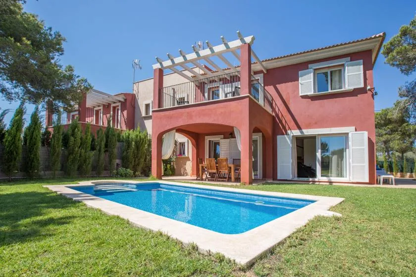A red house with a swimming pool and lawn.