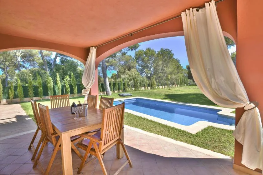 A covered outdoor dining area overlooks a swimming pool and grassy garden.