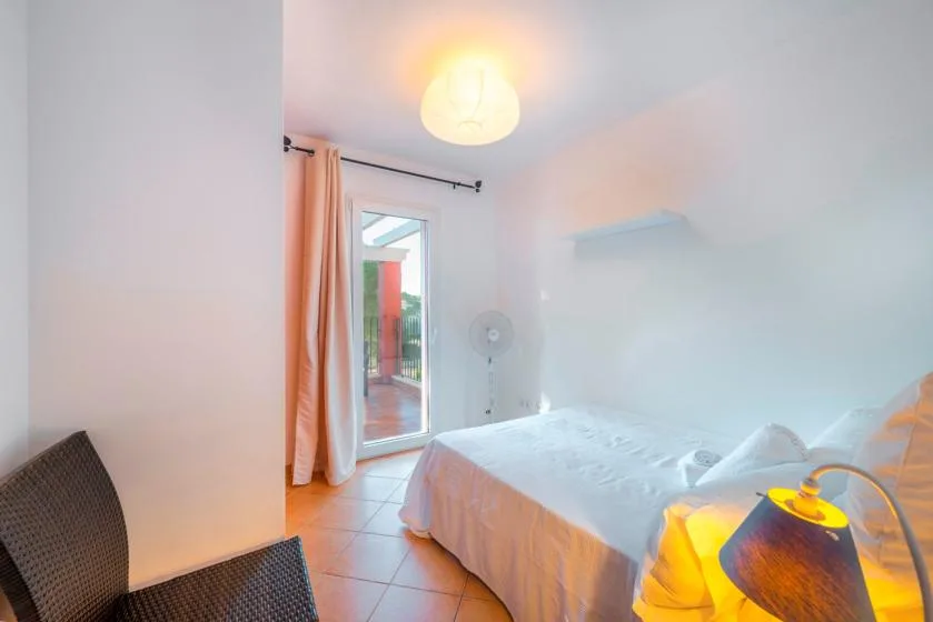A bedroom with a bed, a curtained glass door, and a standing fan.