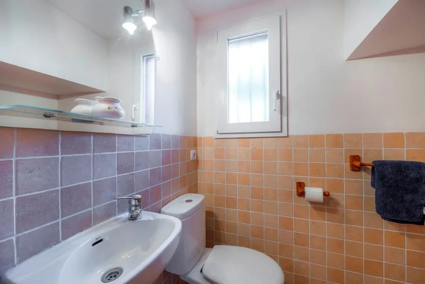 A tiled bathroom with a sink, toilet, and small window.