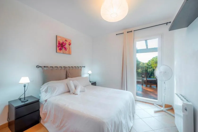 A bright bedroom with a neatly made bed and a glass door opening onto a balcony.