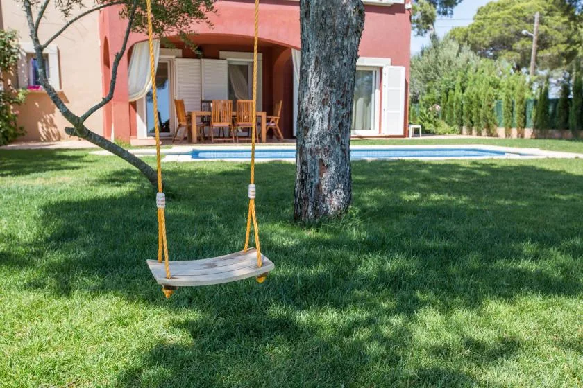 A grassy yard with a hanging swing, swimming pool, and house in the background.