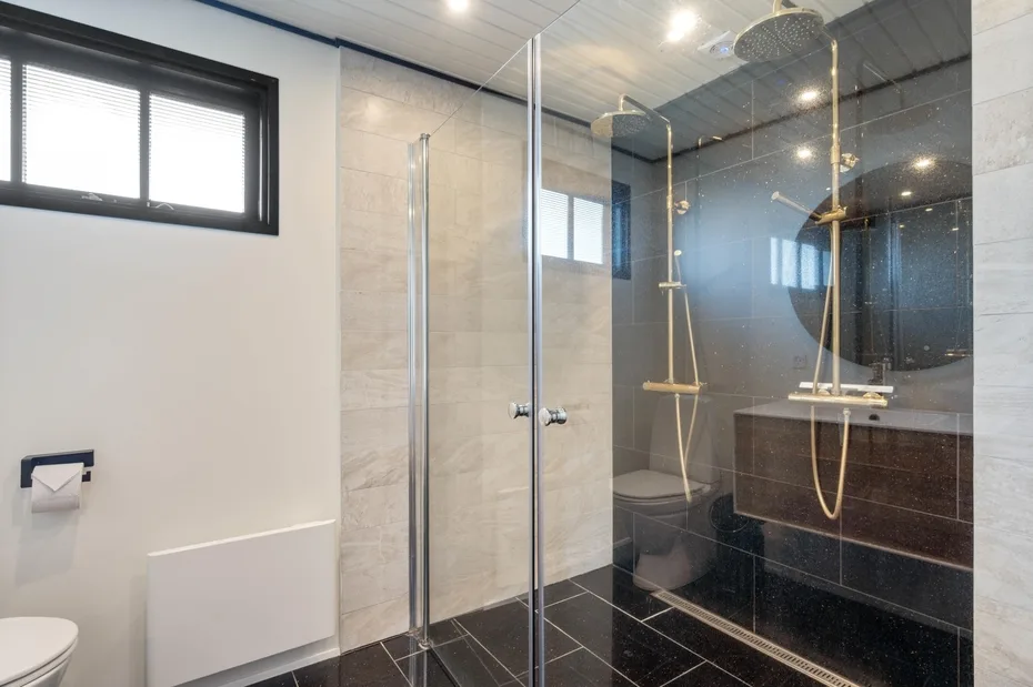 A modern bathroom with a glass shower and dark tiled walls.