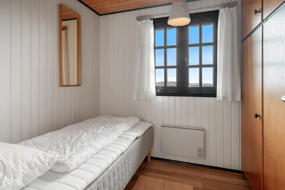 A bedroom with a bed beneath a window with white curtains.