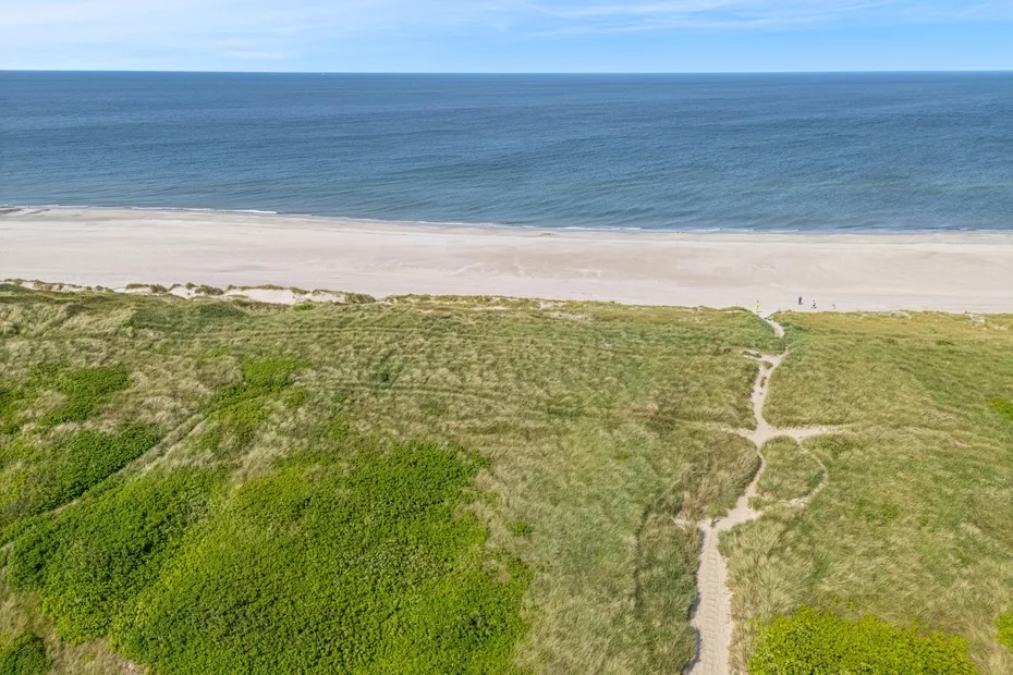 A sandy beach borders the ocean, with grassy dunes and a path in the foreground.