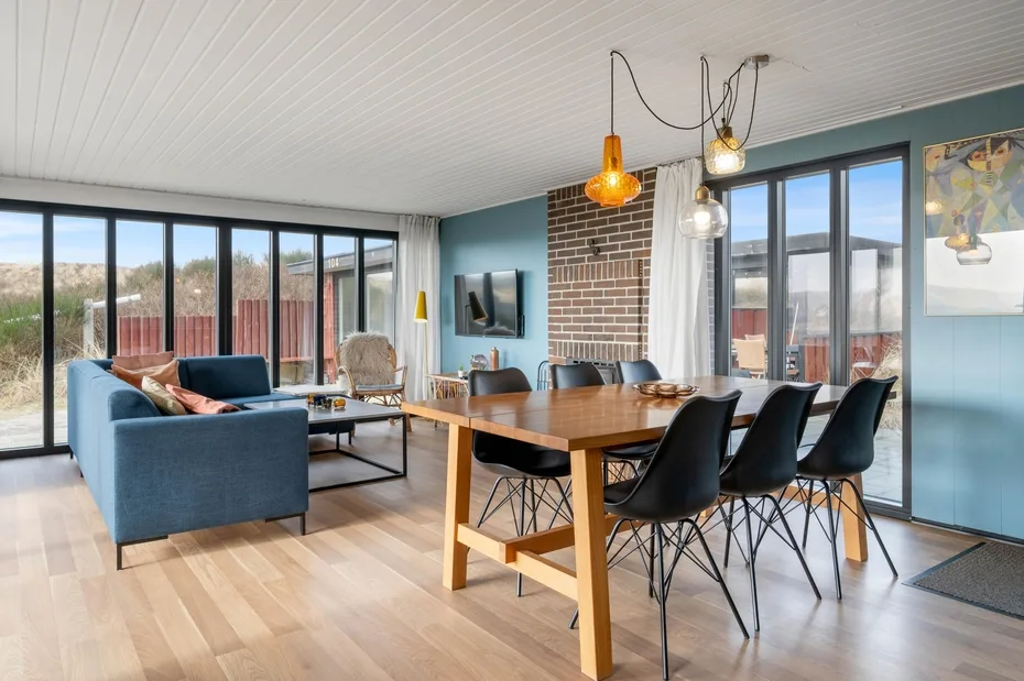 A bright open-plan living and dining area with a table beside large windows.