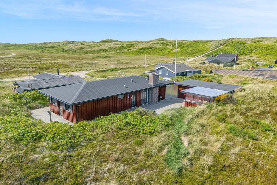 A modern house sits among grassy dunes beneath a clear sky.