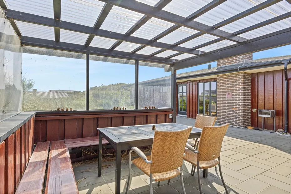 A covered patio with a dining table, seating, and brick walls.