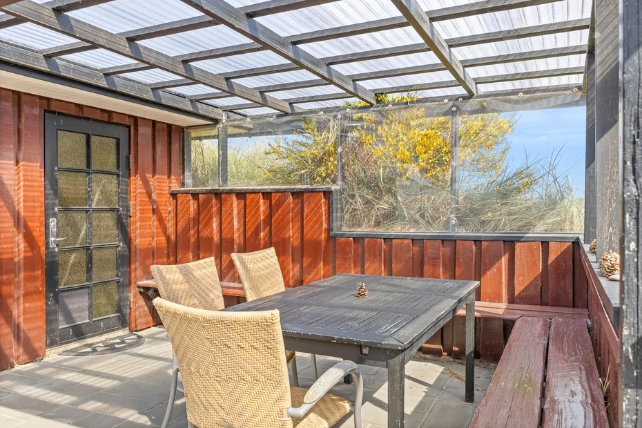 A covered outdoor dining area with a table and seating beneath a translucent roof.