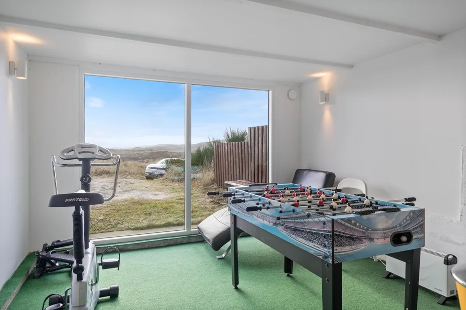 A recreation room with a foosball table and exercise equipment beside large windows.