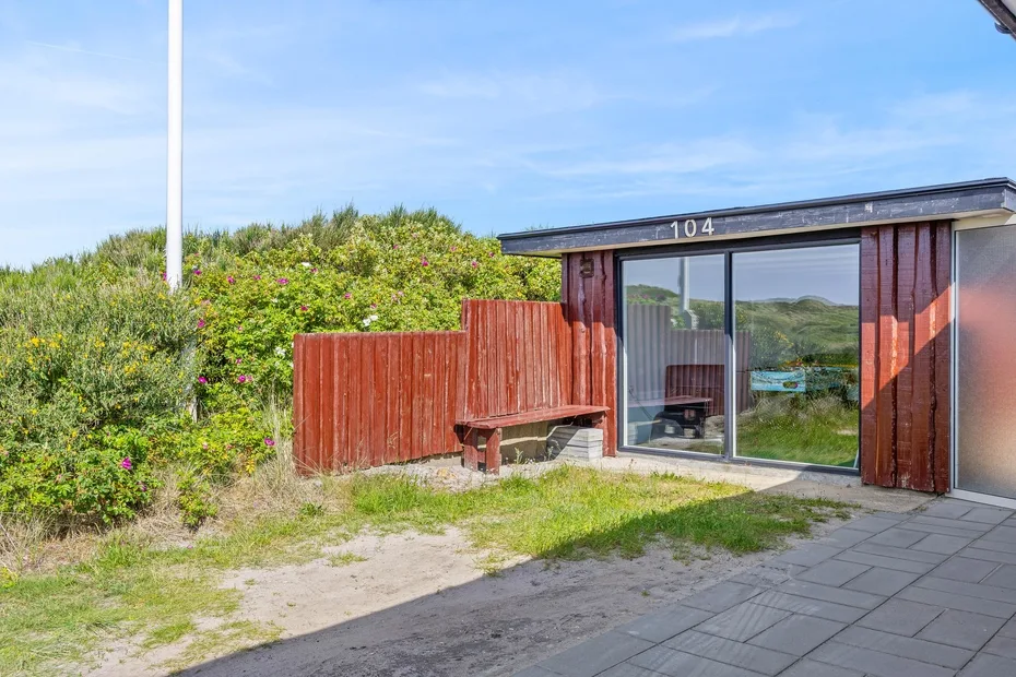 A low building with glass doors sits beside a red wooden fence and green shrubs.