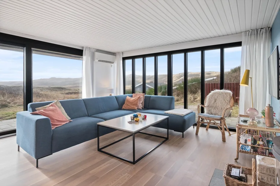 A bright living room has blue seating and large windows overlooking a hilly landscape.