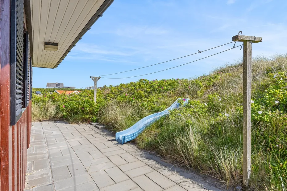 A paved outdoor walkway runs beside grassy dunes and a blue slide.
