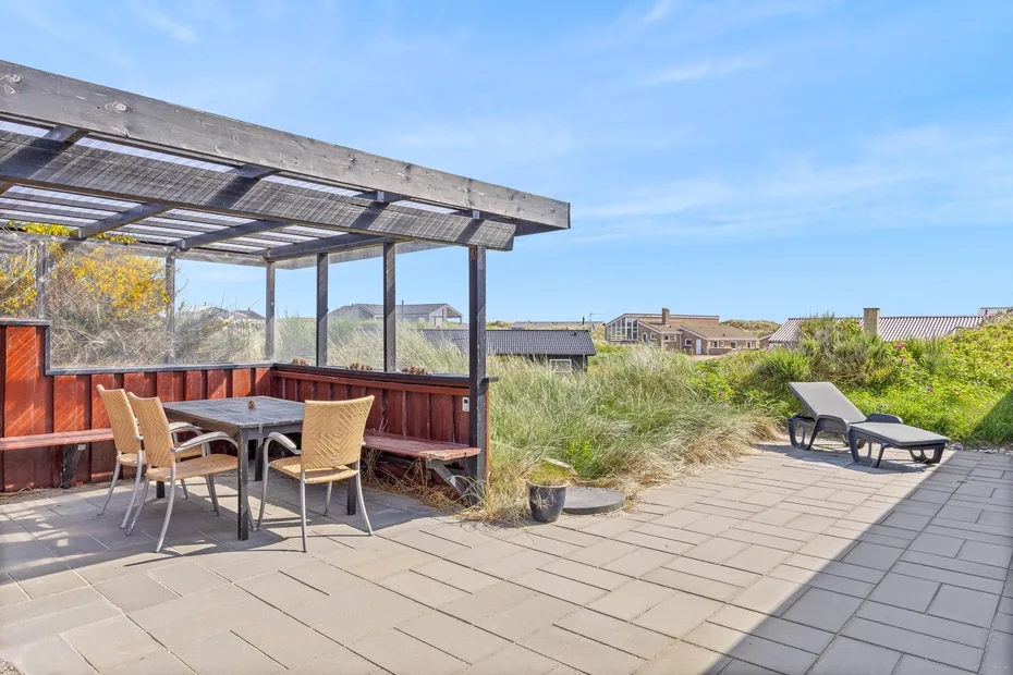 A patio dining area beside a paved terrace, with outdoor seating and loungers.