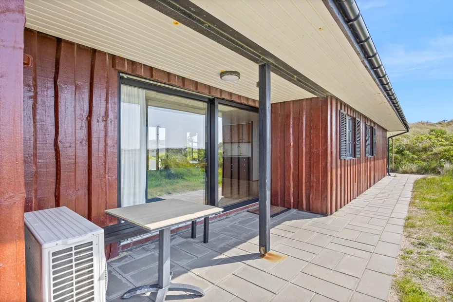 A covered patio runs along a building with sliding glass doors and outdoor seating.