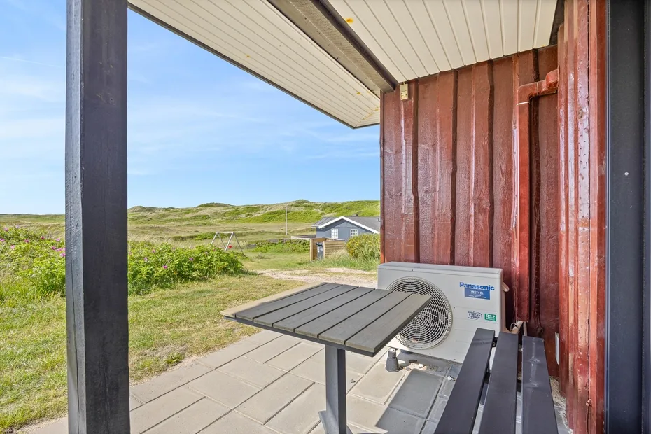 A covered outdoor patio overlooks grassy dunes and a small building.