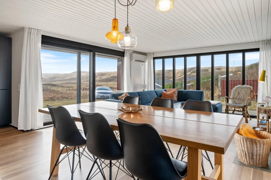 A bright dining area with a long table and large windows overlooking rolling hills.