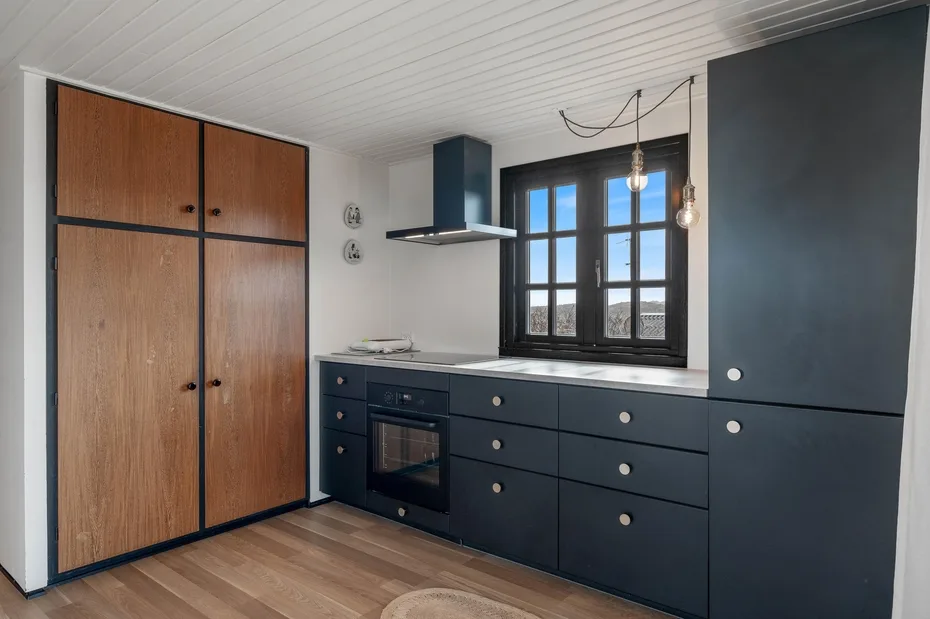 A modern kitchen with dark cabinetry, a built-in oven, and a window.