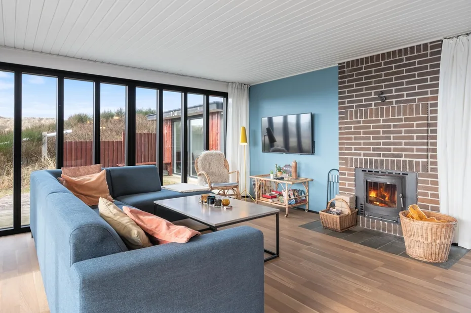 Living room with seating, a television, and a fireplace beside large windows.
