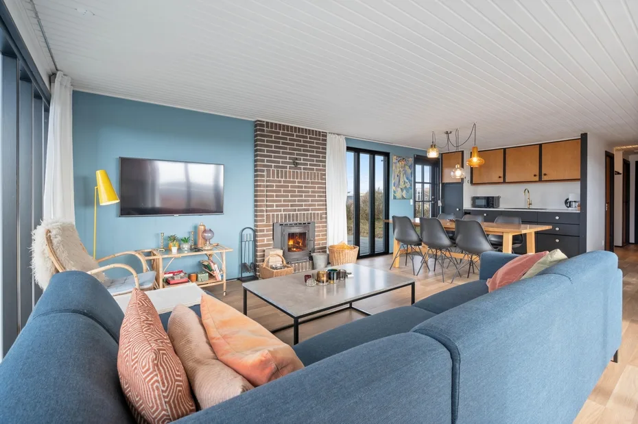 A living room with blue seating, a fireplace, and an open kitchen.