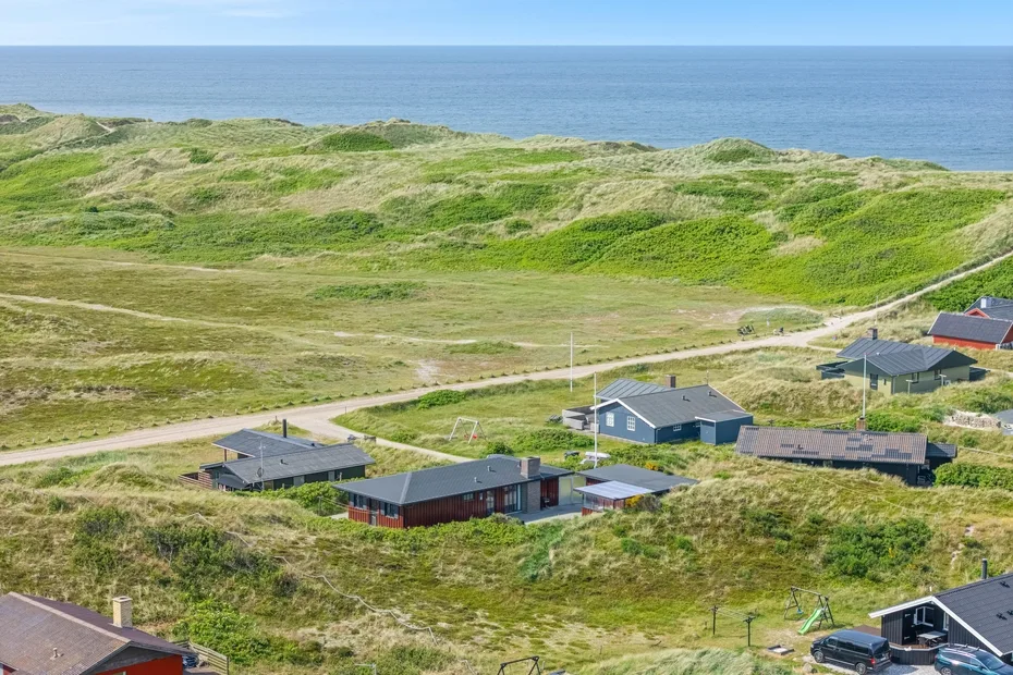 Coastal landscape with houses among grassy dunes beside the sea.