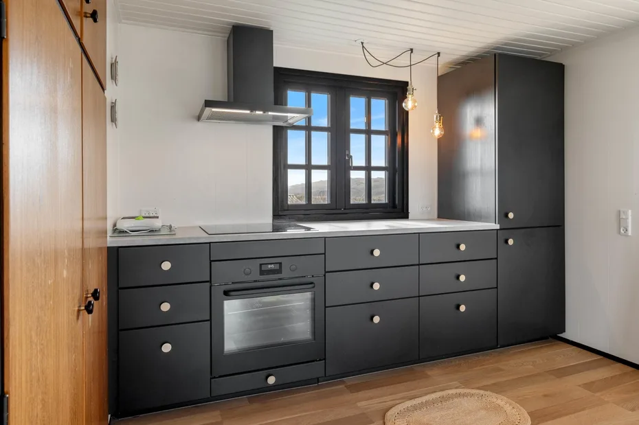 A modern kitchen with dark cabinets, a built-in oven, and a large window.