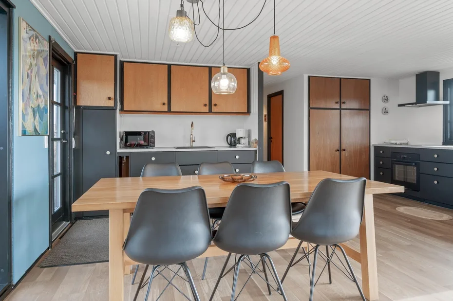 A dining area with a wooden table and a kitchen in the background.