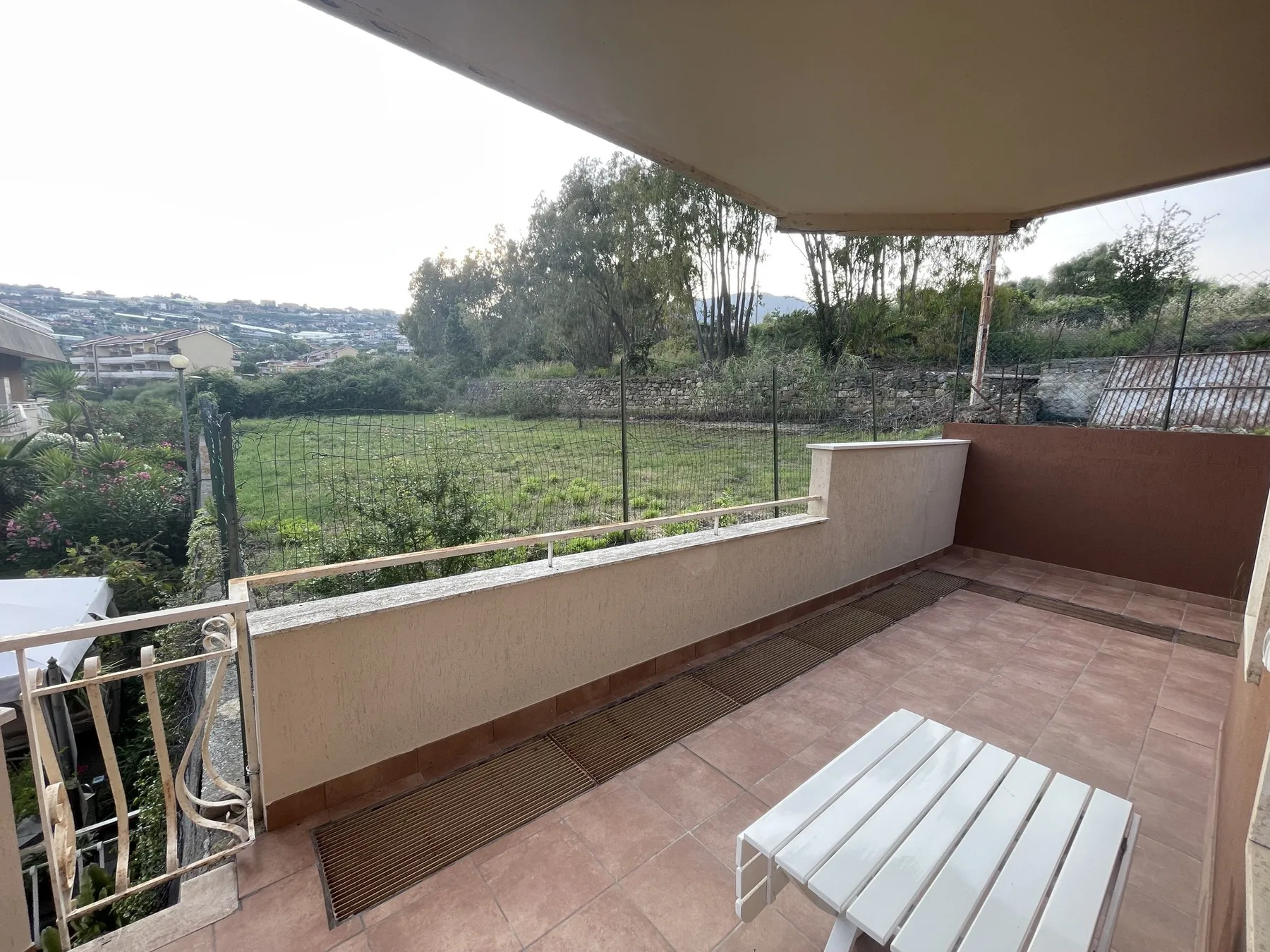 Un patio cubierto da a un campo verde y casas en una ladera cercana.