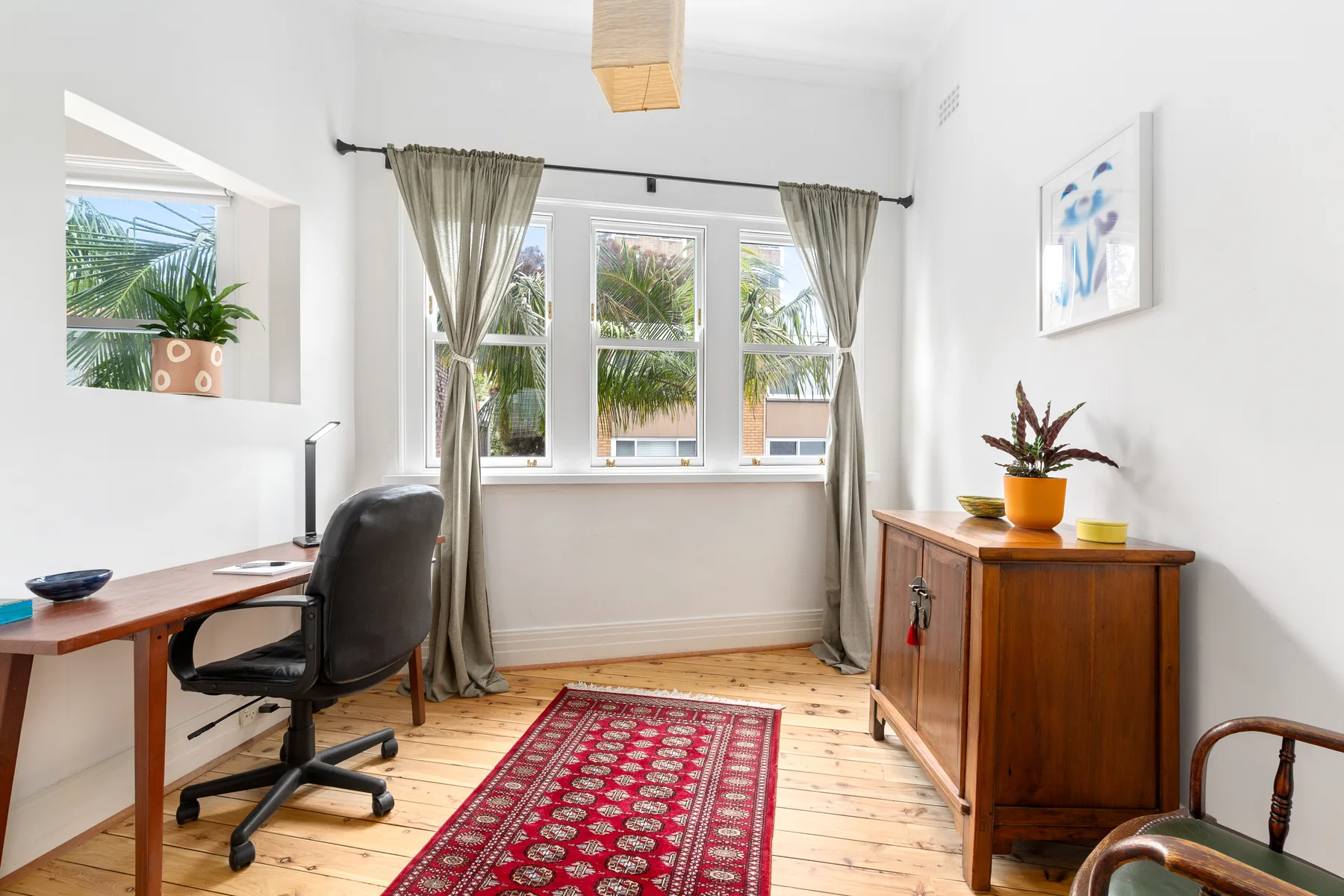 Un espacio de trabajo luminoso con escritorio, silla de oficina y ventanas con vistas a la vegetación.