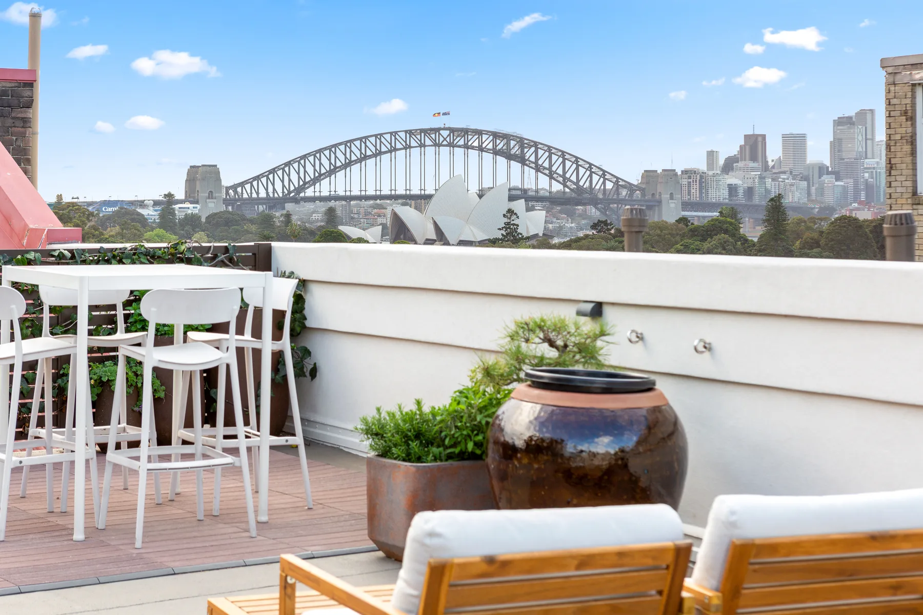 A rooftop terrace overlooks Sydney Harbour, with the Harbour Bridge and Opera House in the distance.