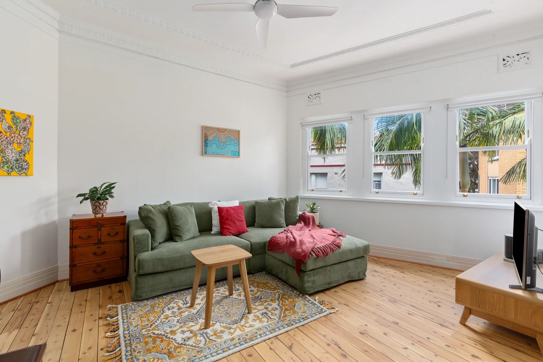 A living room with seating, a television and windows overlooking greenery.