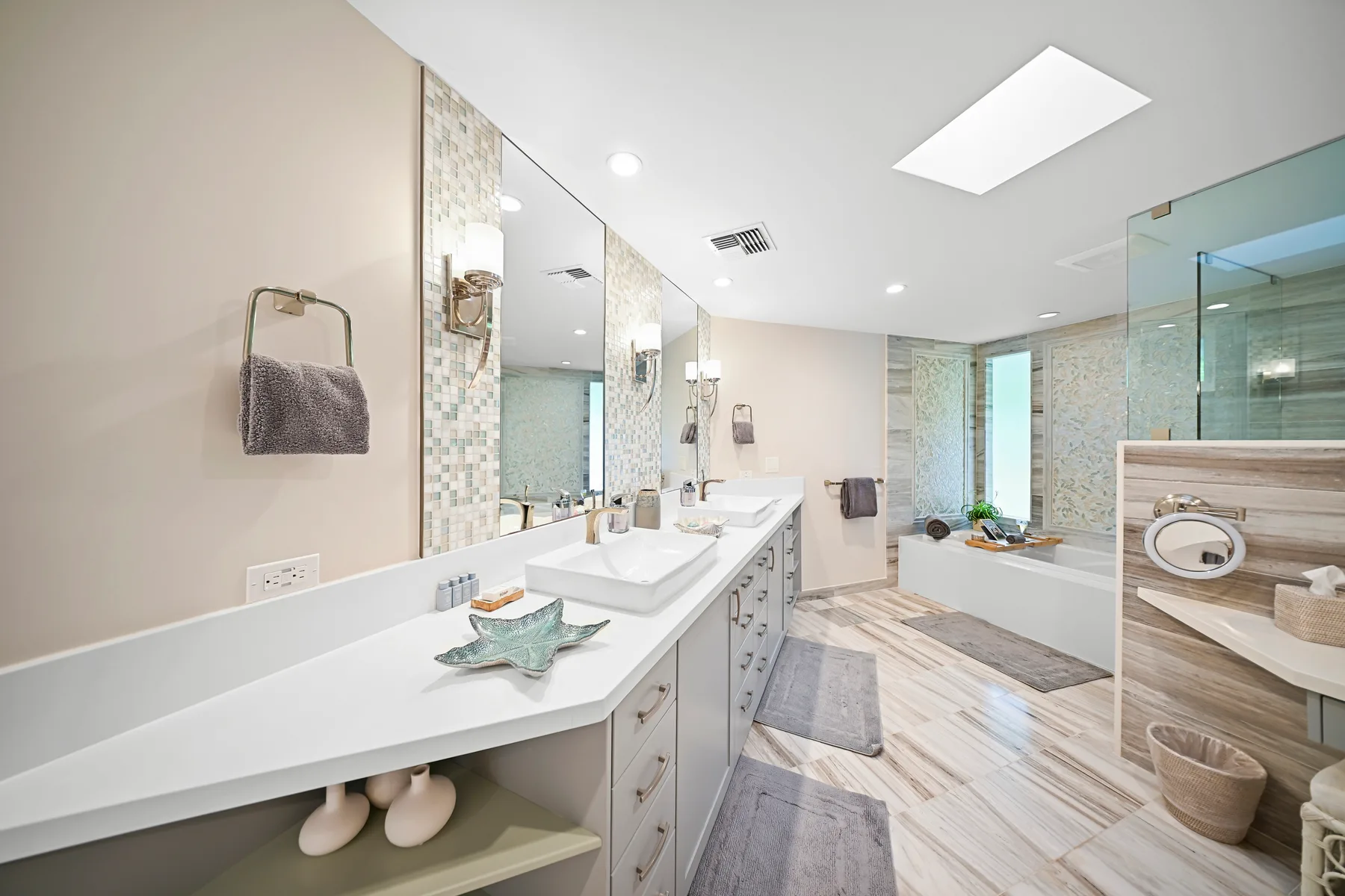 A bright bathroom with a long vanity, sinks, and a glass shower.