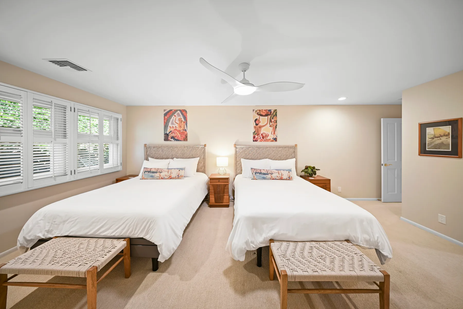 A bright bedroom with two beds, bedside tables, and wide windows.