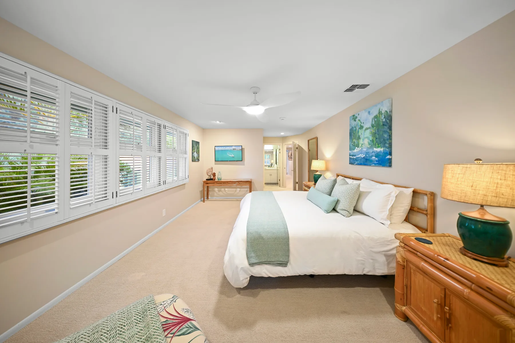 A bedroom with a large bed, wide windows, and a wooden dresser.