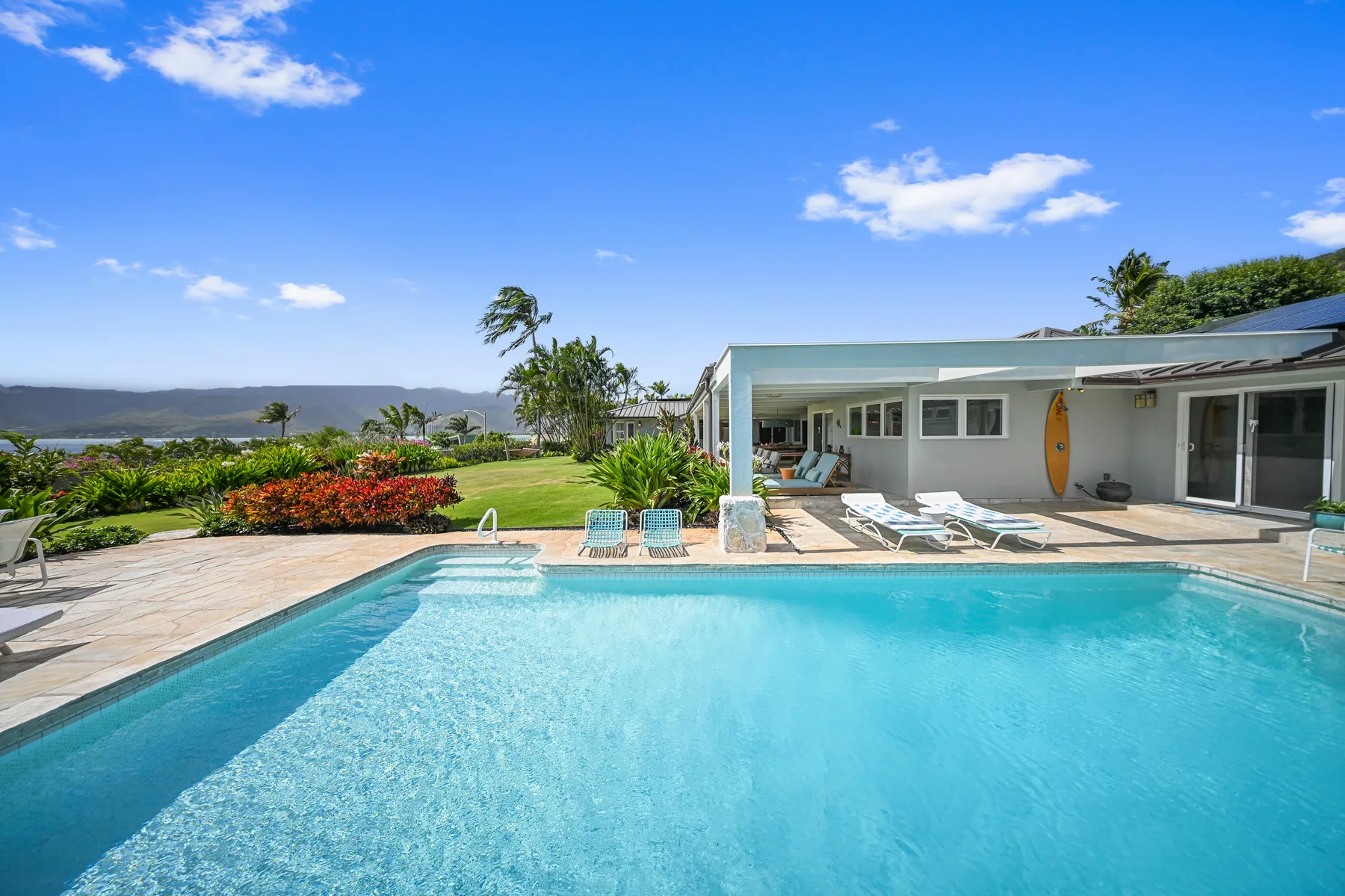 Outdoor swimming pool beside a low house, with lounge seating and landscaped grounds.
