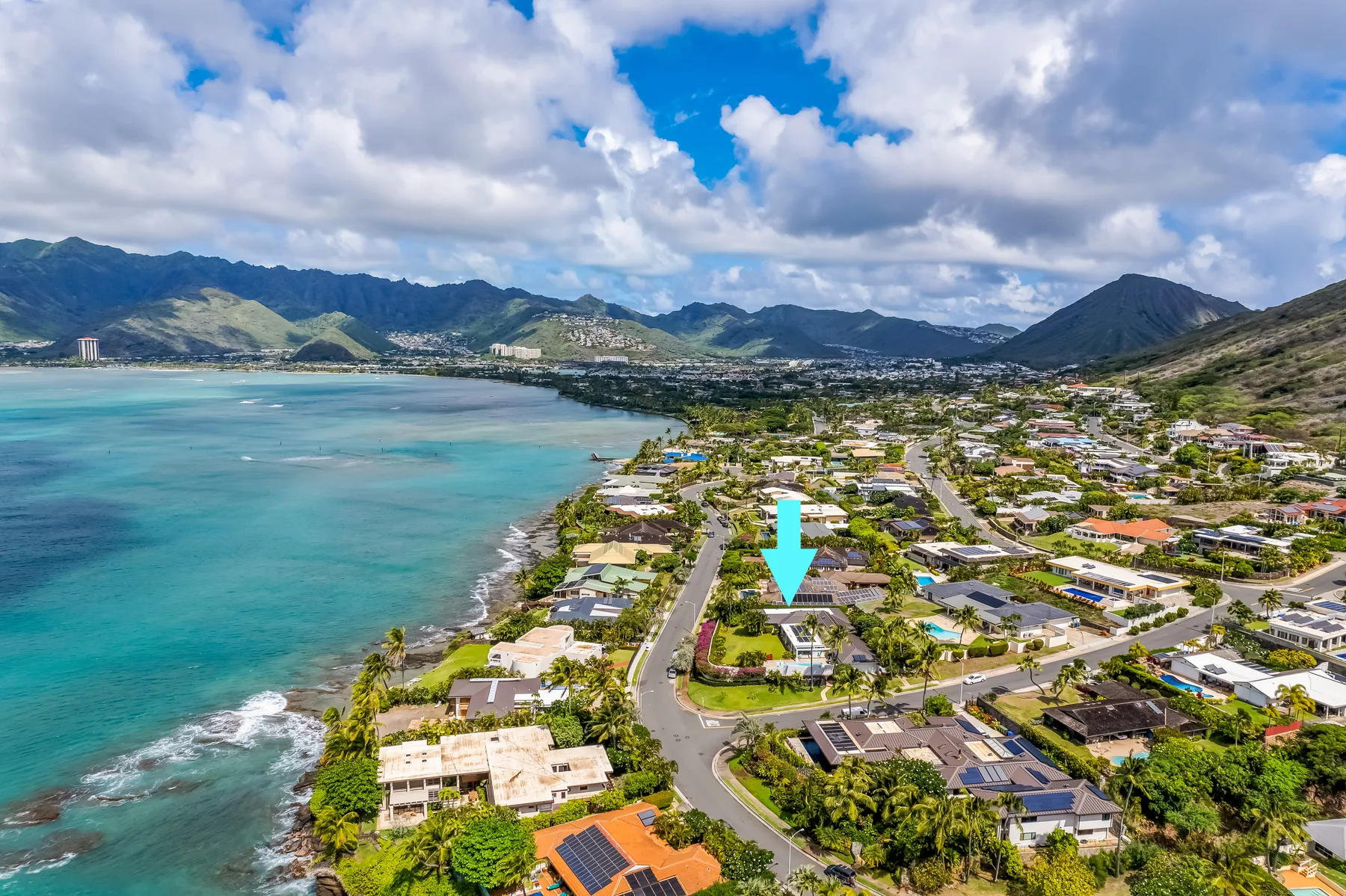 Aerial view of a coastal neighborhood beside turquoise water and distant mountains.