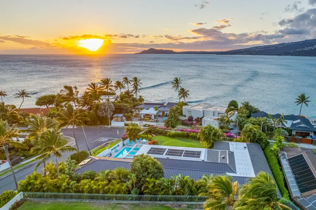 Aerial view of a coastal resort with a pool beside the ocean at sunset.