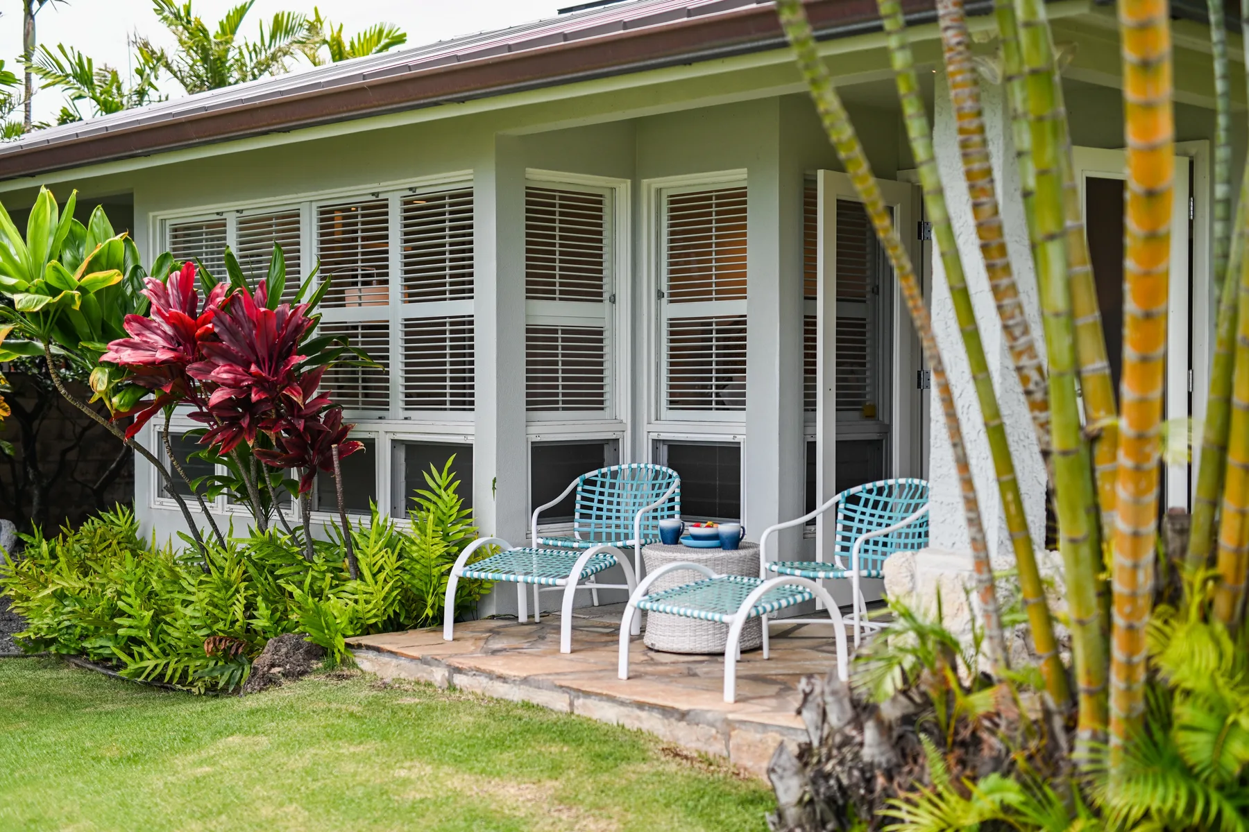 A small covered patio with metal seating overlooks a garden.