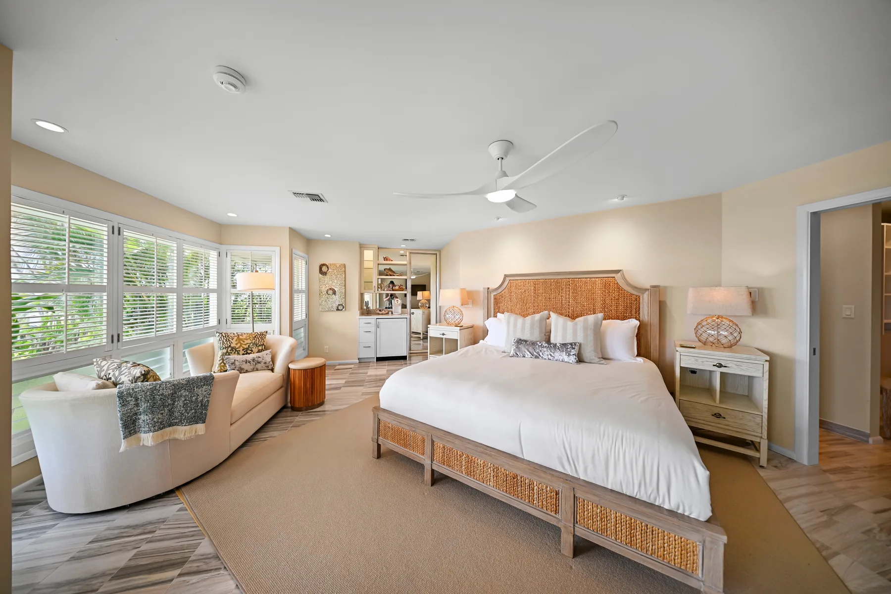A bright bedroom with a large bed and a seating area beside wide windows.