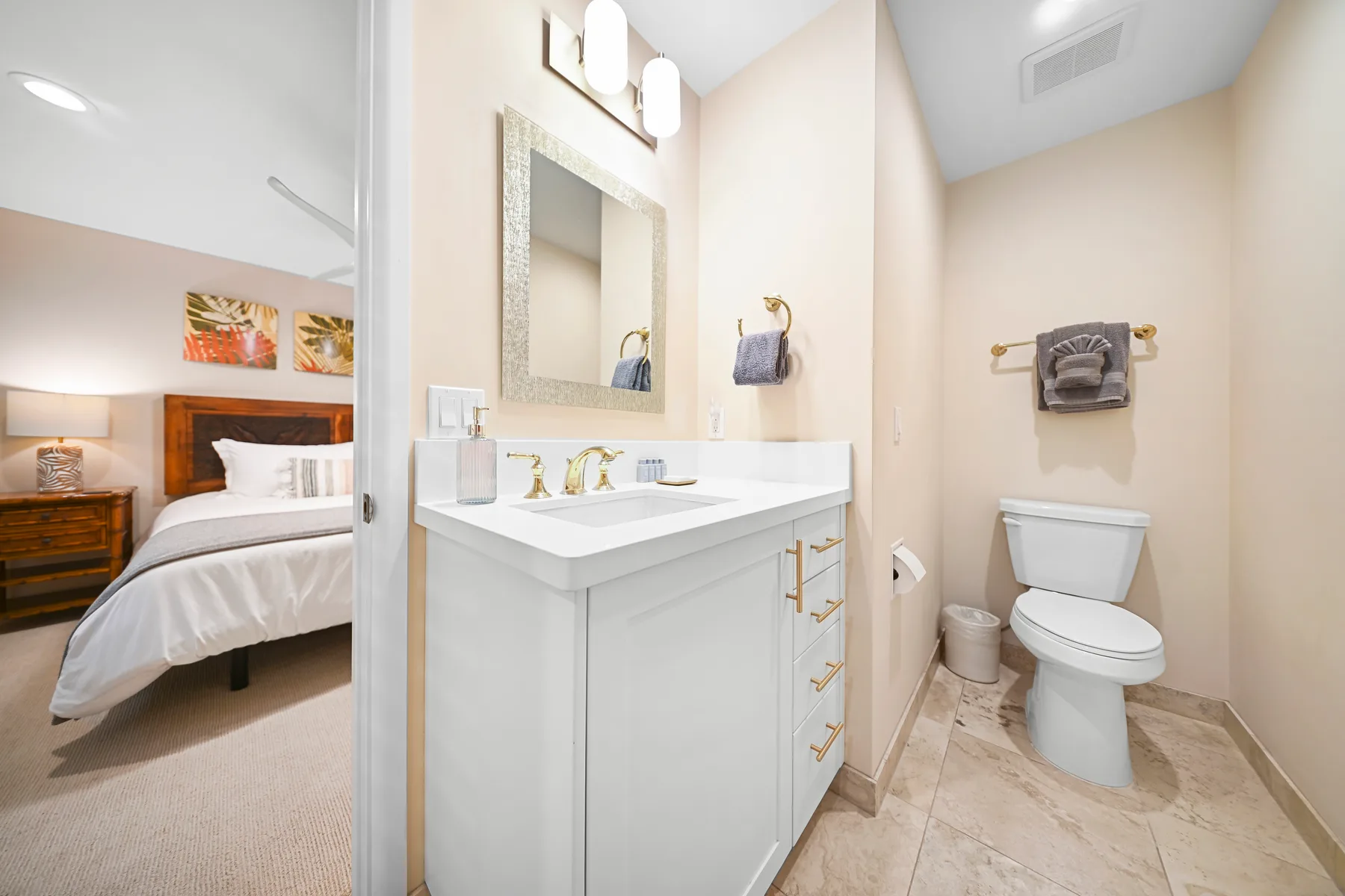 A bathroom with a vanity and toilet, with a bedroom visible through the doorway.