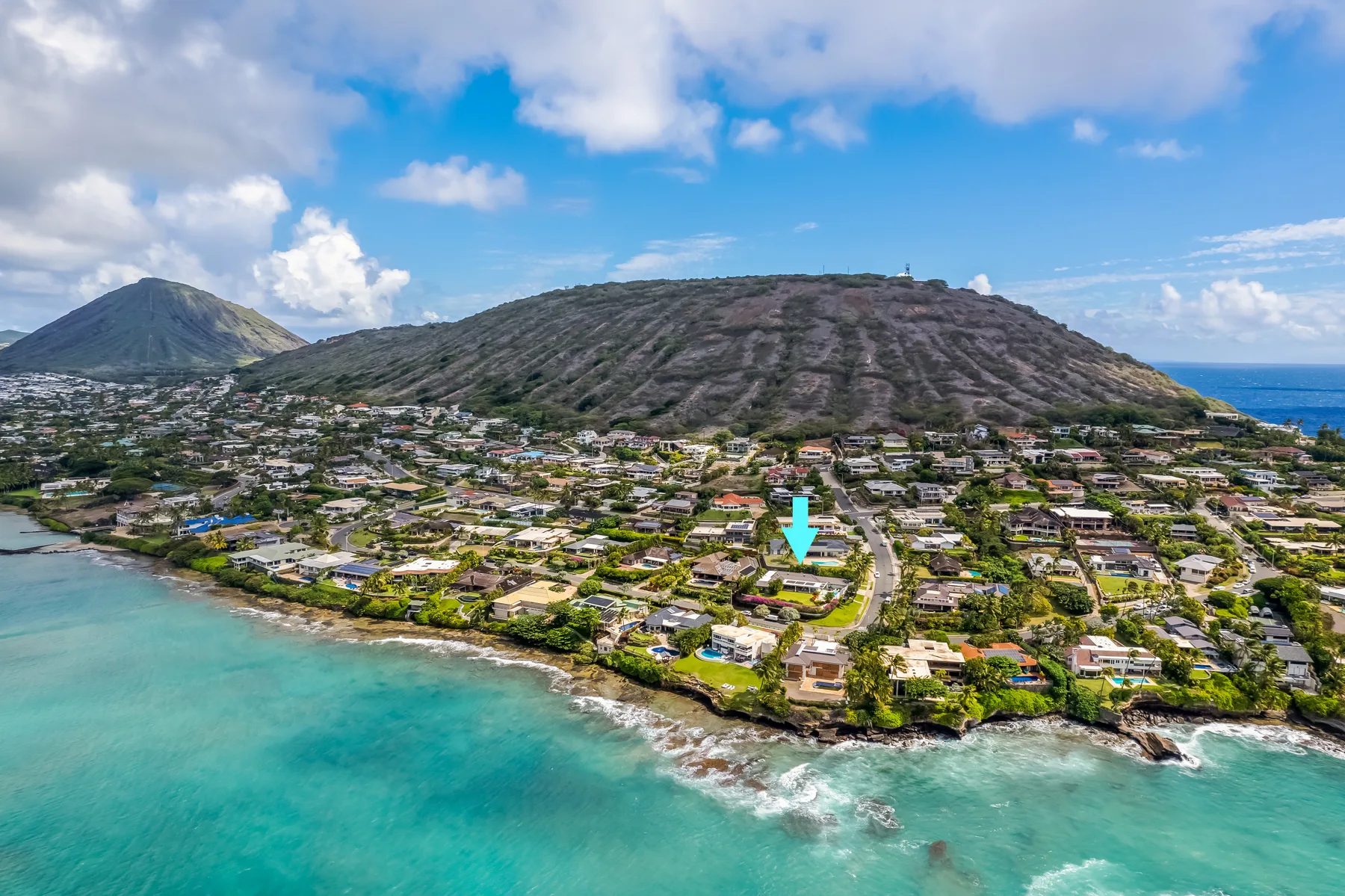 A coastal neighborhood stretches along turquoise water beneath a broad, rugged hillside.