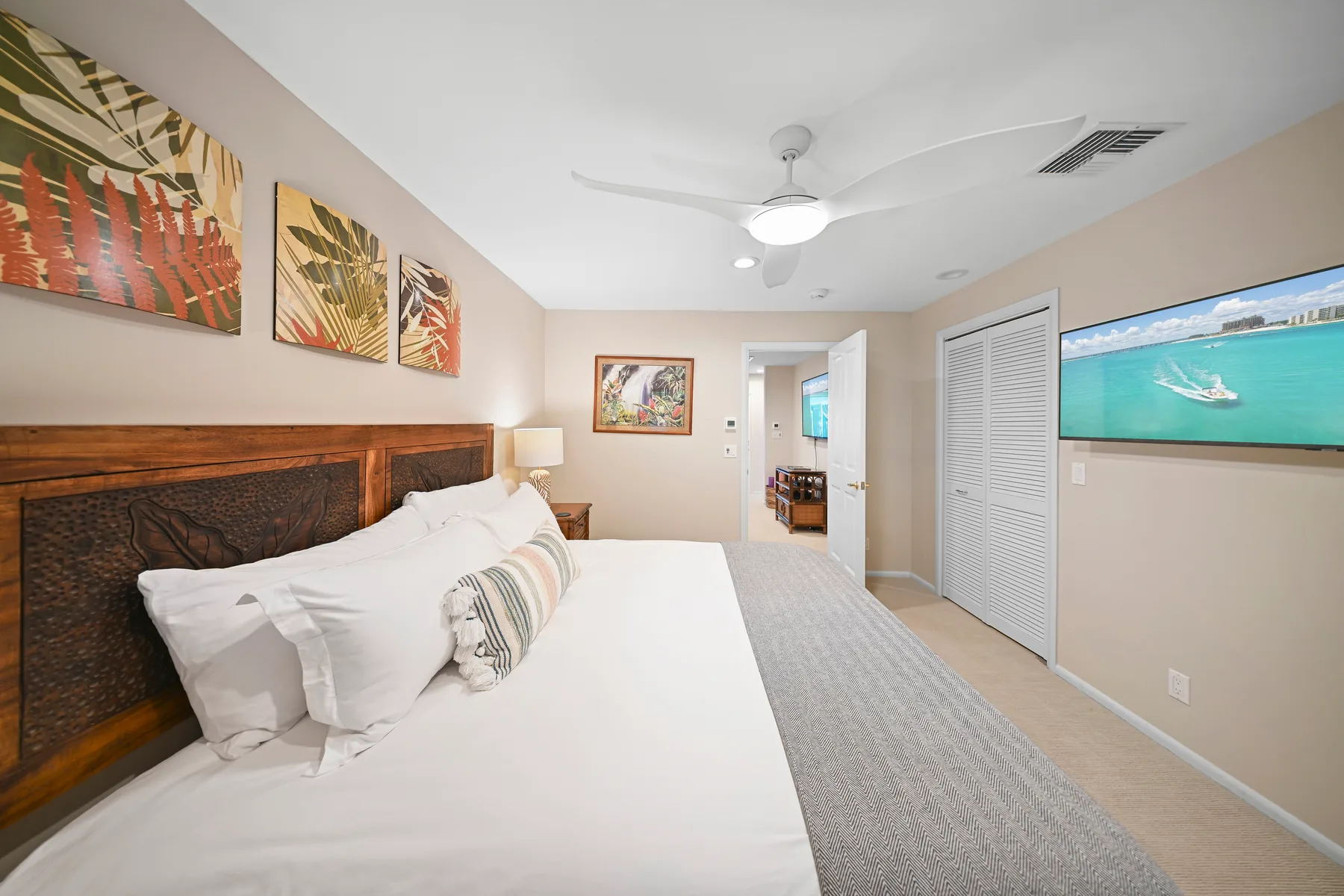 A bedroom with a large bed, framed artwork, and a ceiling fan.