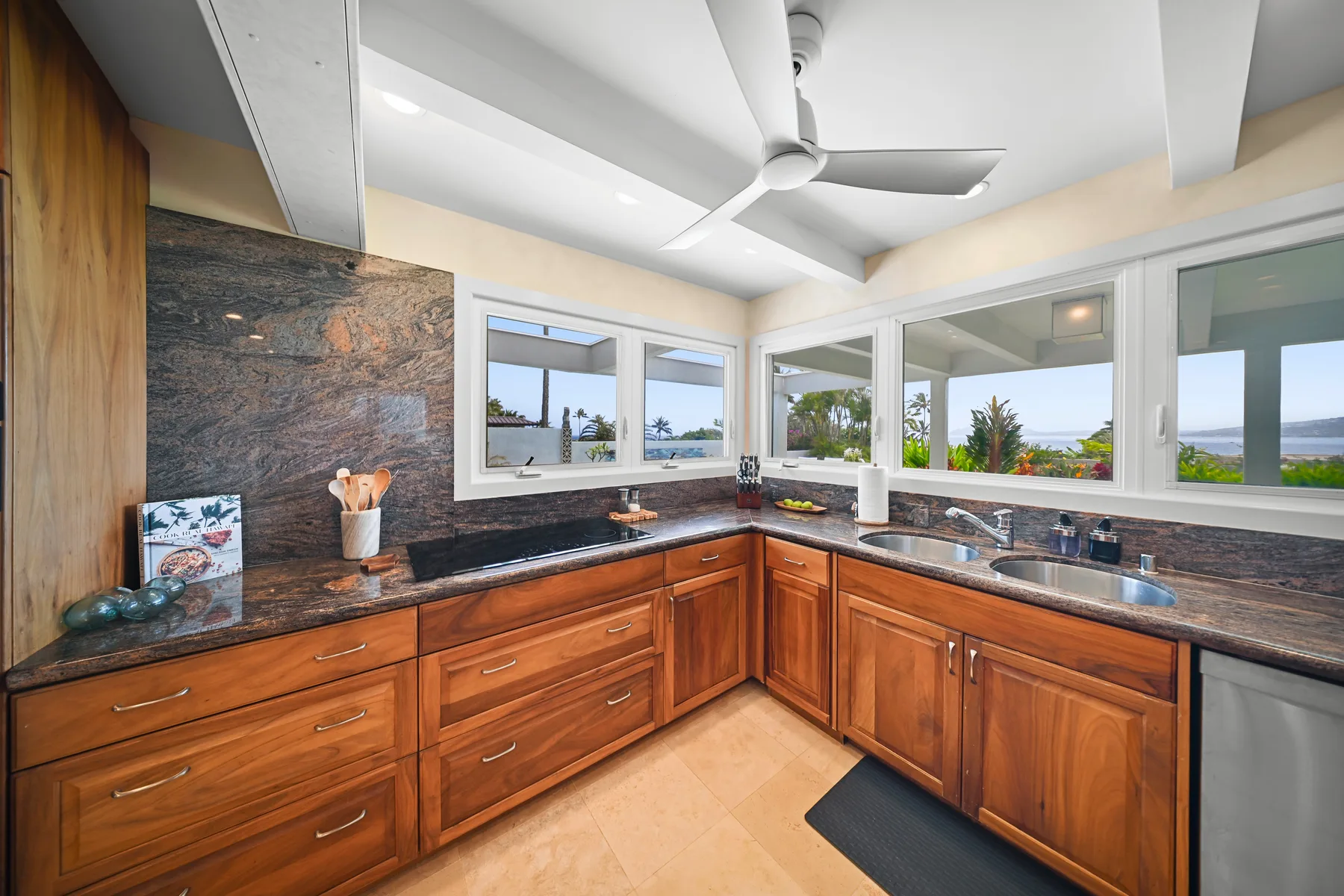 A kitchen with wooden cabinets, dark countertops, and windows overlooking greenery.