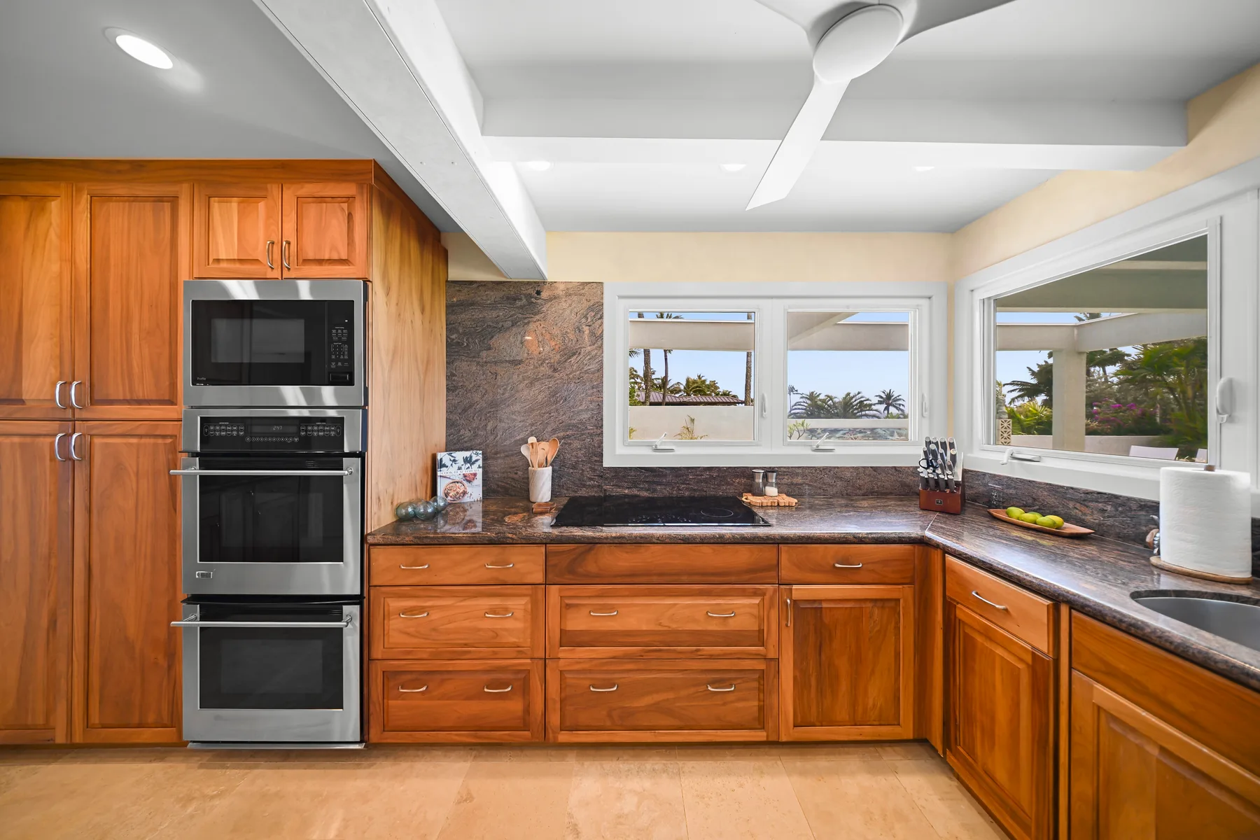 A kitchen with wooden cabinets, dark countertops, and windows overlooking greenery.