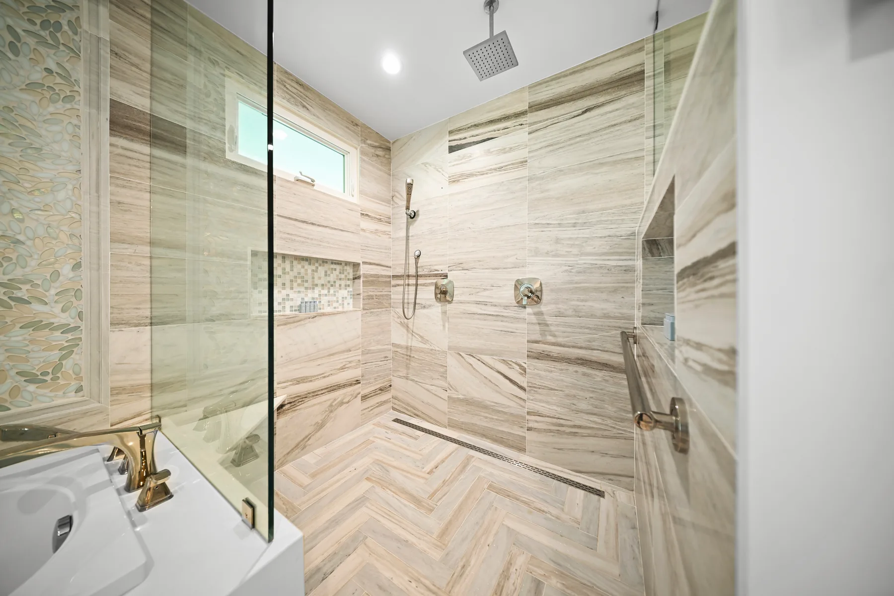A bright tiled bathroom with a glass shower and wall-mounted shower fixtures.
