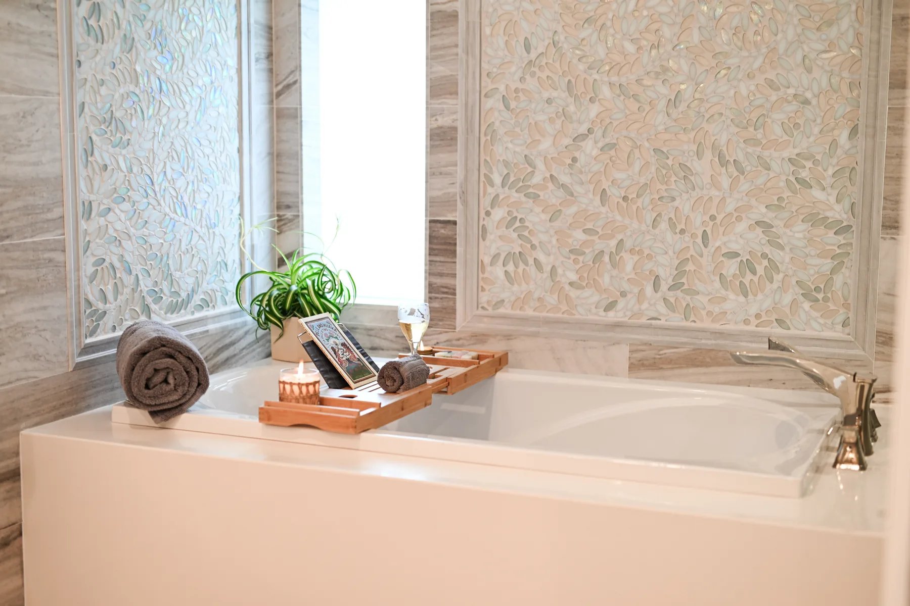 A bathtub sits beneath patterned wall panels, with a tray and plant beside it.