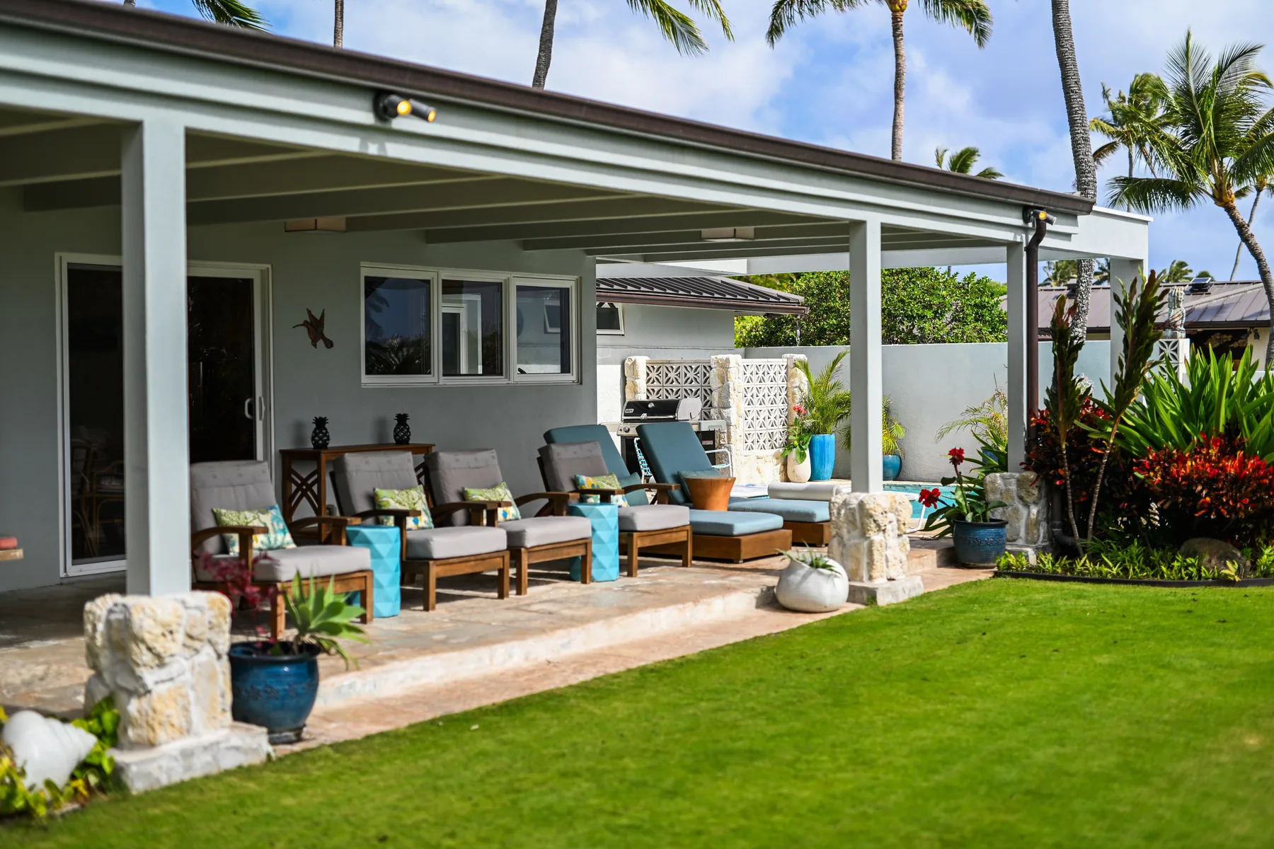 A covered outdoor seating area overlooks a green lawn and tropical garden.