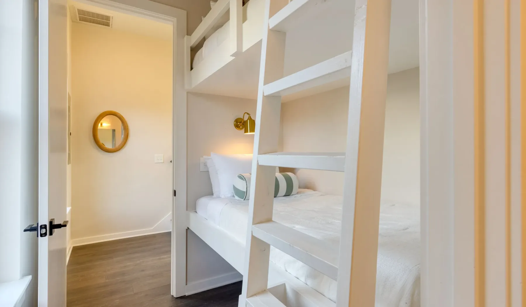 Un dormitorio con literas blancas y un espejo redondo en la pared.