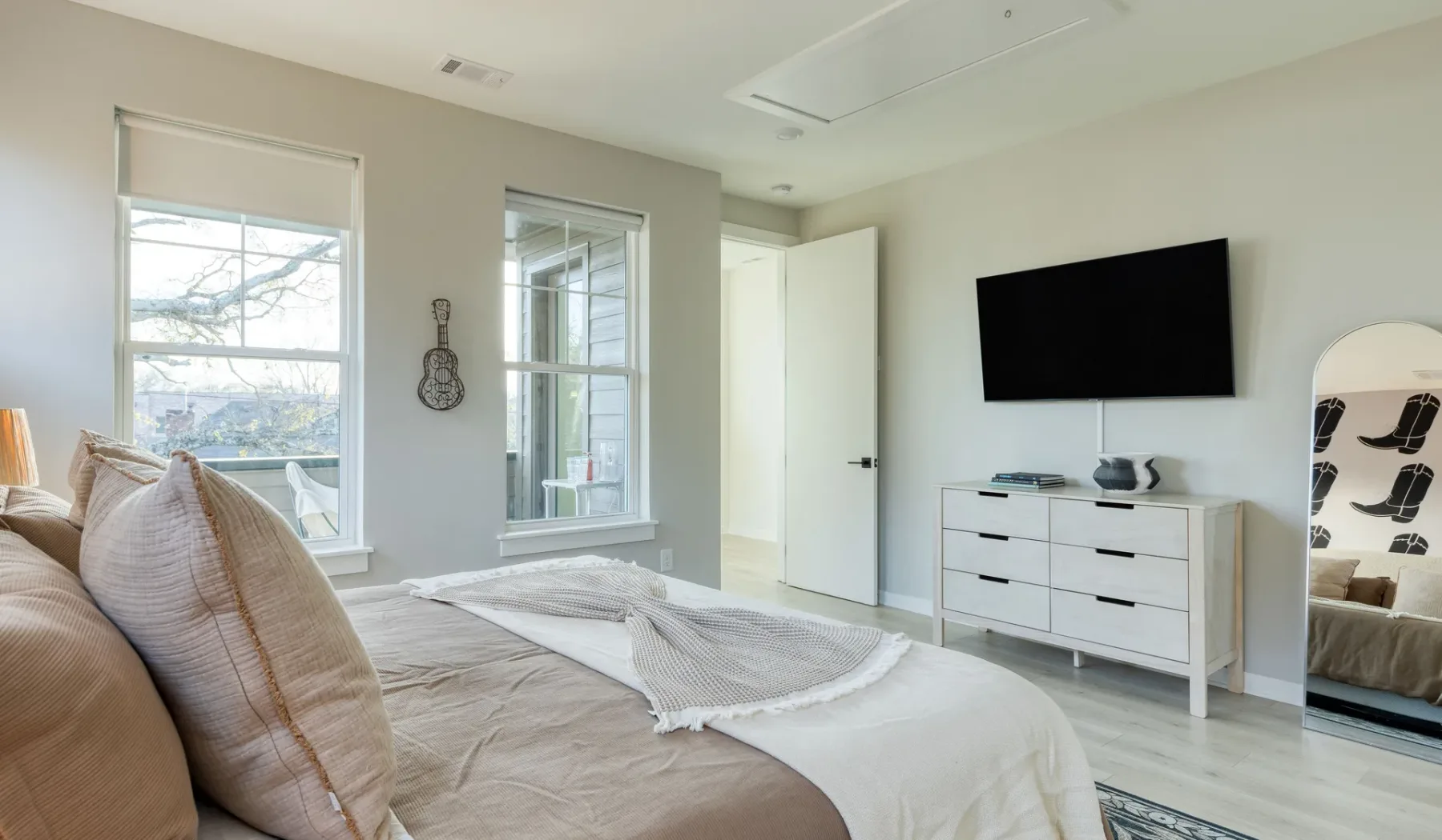 Un dormitorio luminoso con una cama, dos ventanas y un televisor en la pared.